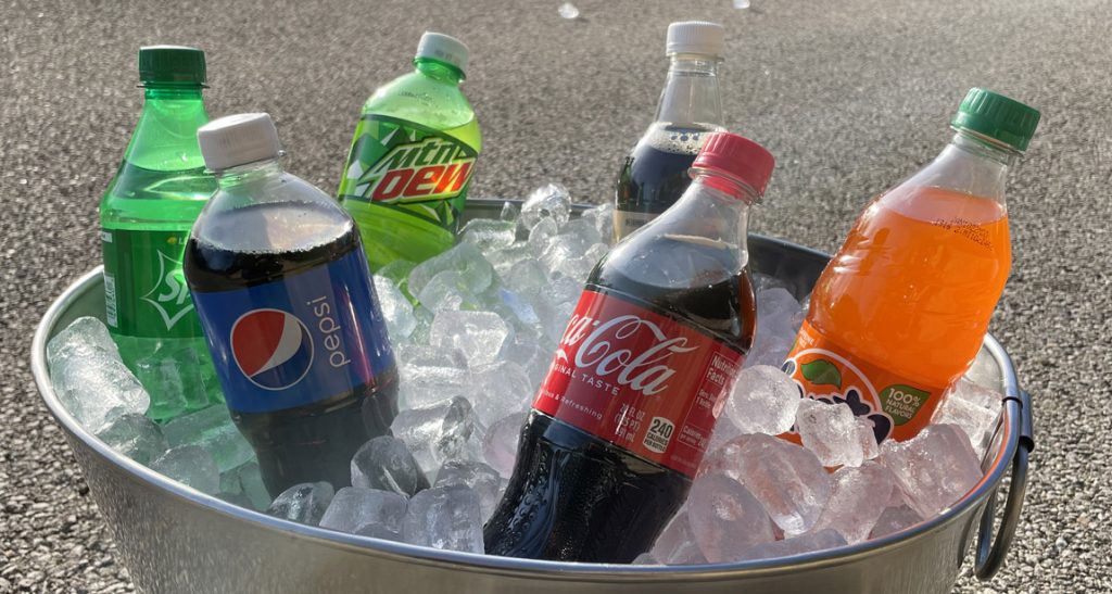 Various bottles of soda surrounded by ice in metal bucket.